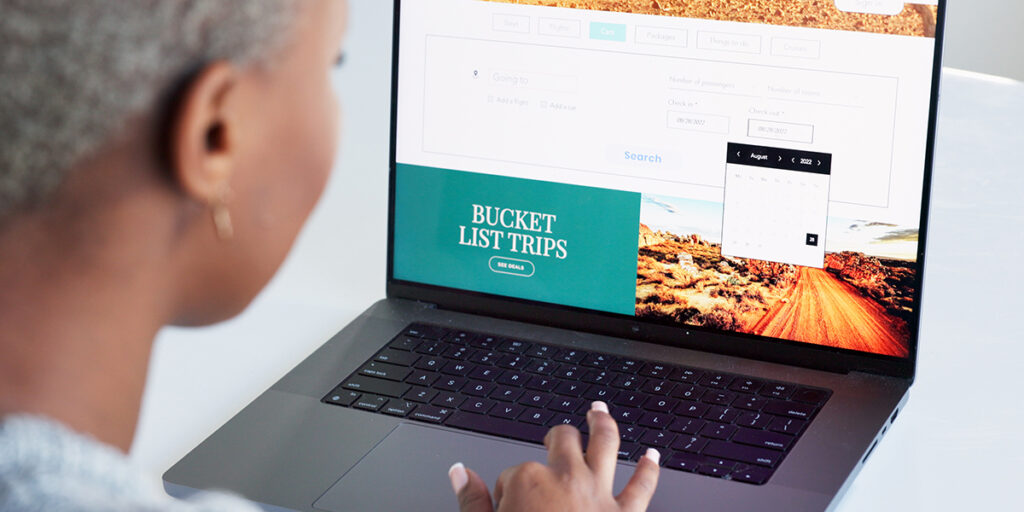 A person using a laptop displaying a travel booking website. The screen shows "Bucket List Trips" with a desert landscape. A calendar widget is visible, suggesting search functionality for choosing travel dates.