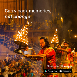 A religious ceremony with people holding flaming torches near a riverbank, attended by a large crowd. Text reads, "Carry back memories, not change." App download icons for Google Play and App Store are visible.
