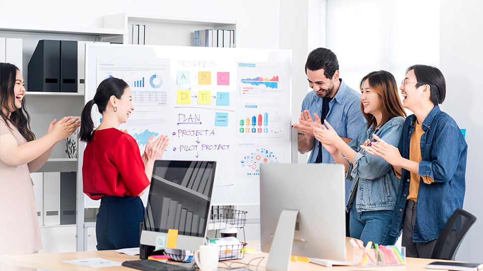 A team of people collaborates around a whiteboard, actively discussing and writing down their thoughts and plans.